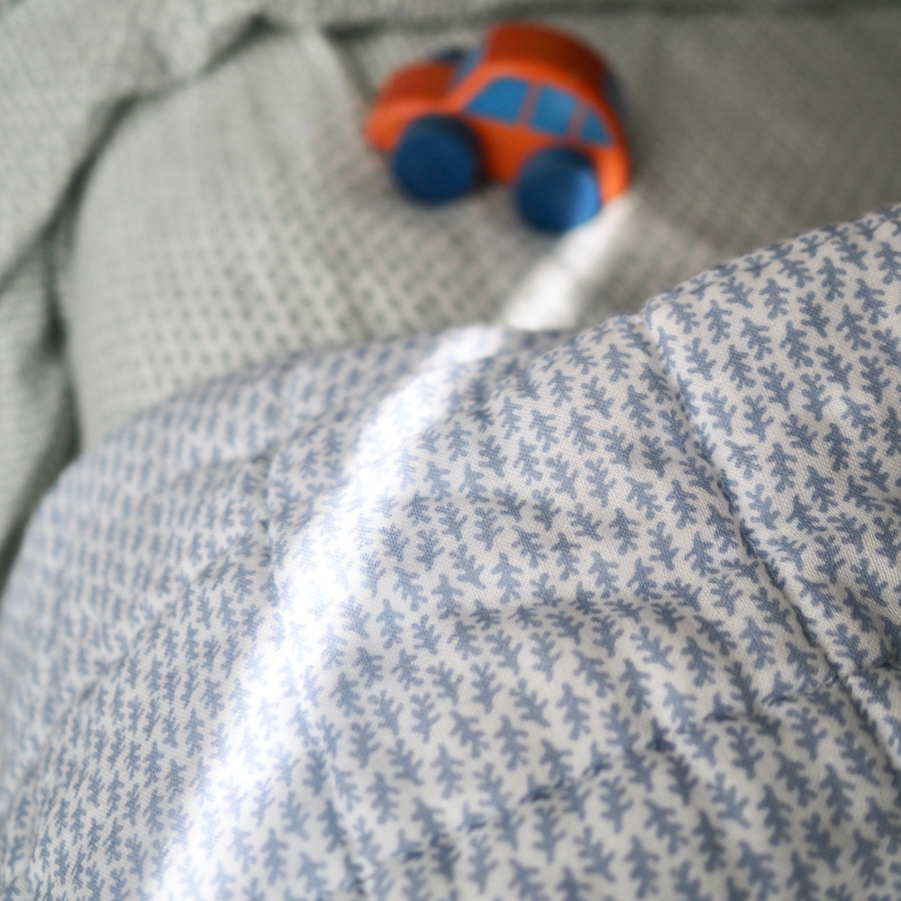 Gros plan sur la couverture matelassée pour enfant en mousseline de coton Candide Living de motif Ondine en bleu chambray.