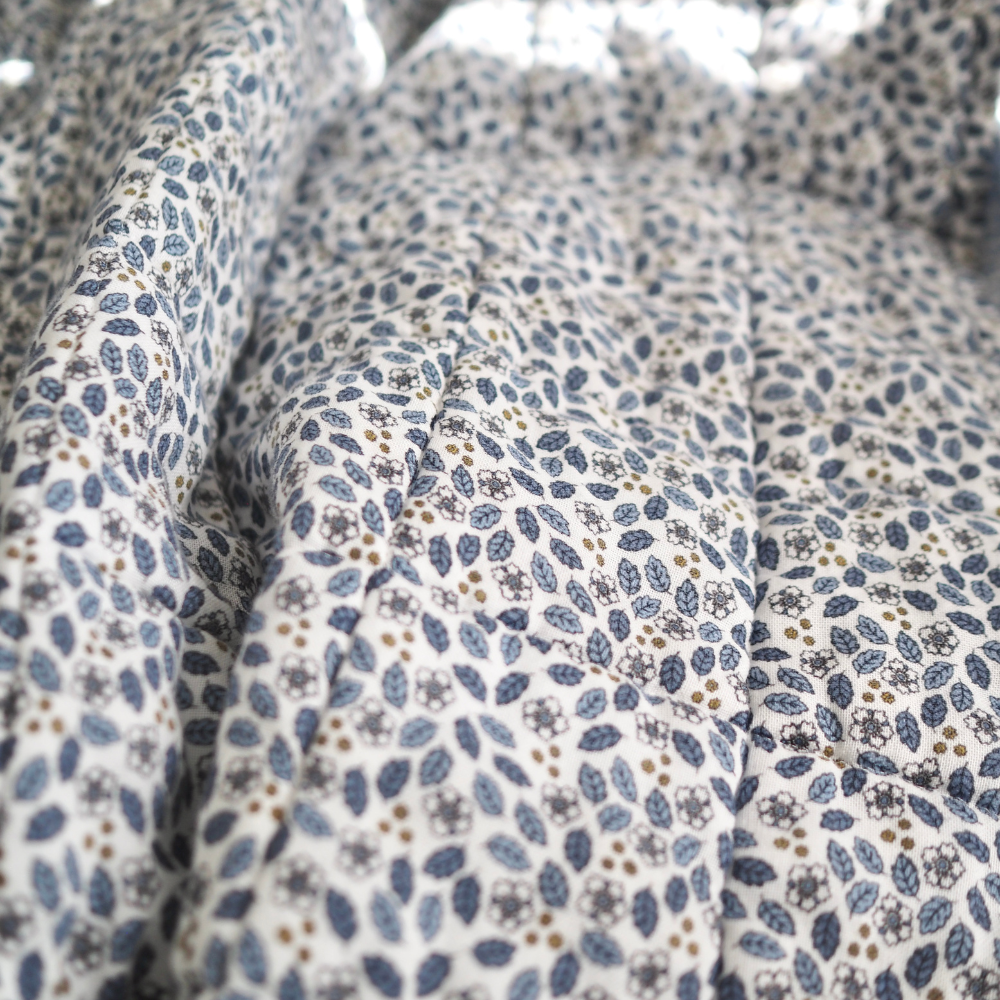 Gros plan sur la couverture matelassée pour enfant en mousseline de coton Candide Living de motif Flora en bleu chambray.