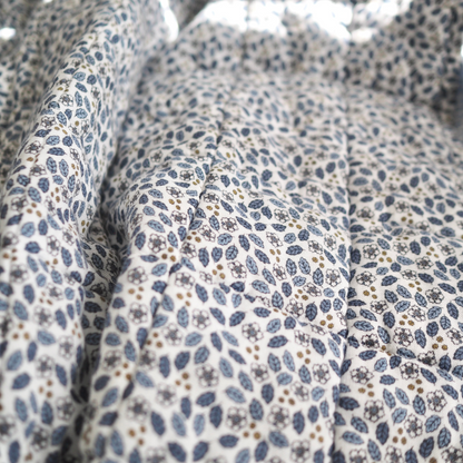 Gros plan sur la couverture matelassée pour enfant en mousseline de coton Candide Living de motif Flora en bleu chambray.