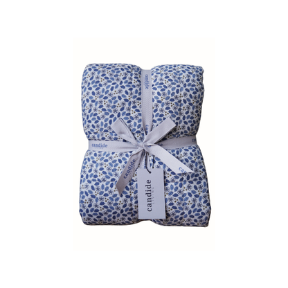 Couverture matelassée pour enfant en mousseline de coton Candide Living de motif Flora en bleu chambray présentée avec ruban. 
