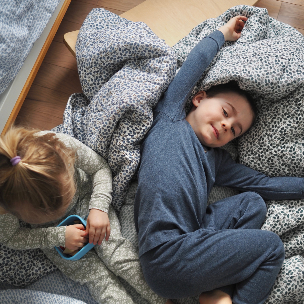 Couverture matelasse pour enfants en mousseline de coton Candide Living dans nos deux teintes disponibles - vert sauge et bleu chambray - sur le plancher avec 2 enfants. 