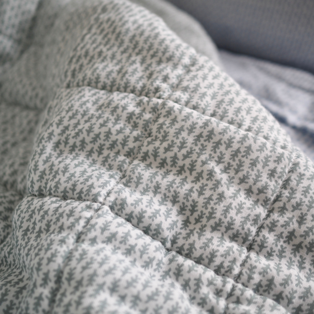 Gros plan sur la couverture matelassée pour enfant en mousseline de coton Candide Living de motif Ondine en vert sauge.