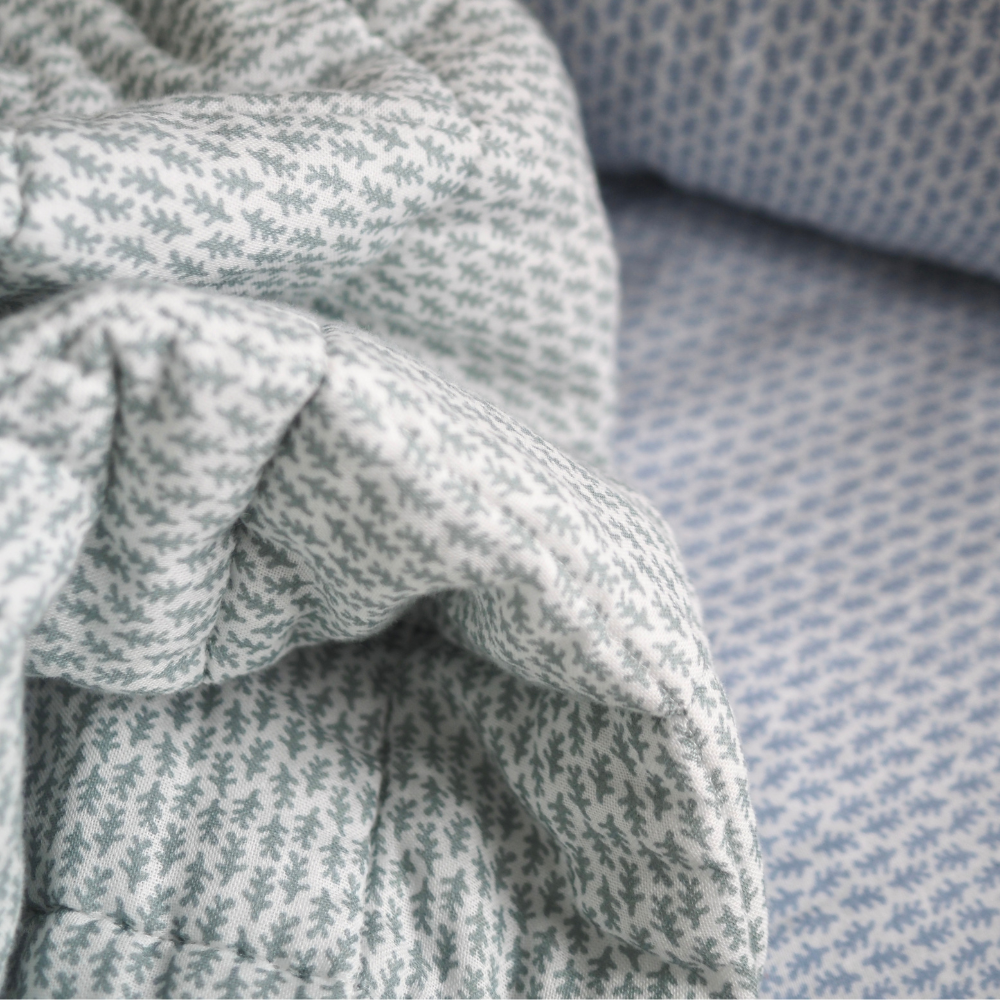 Gros plan sur la couverture matelassée pour enfant en mousseline de coton Candide Living de motif Ondine en vert sauge.