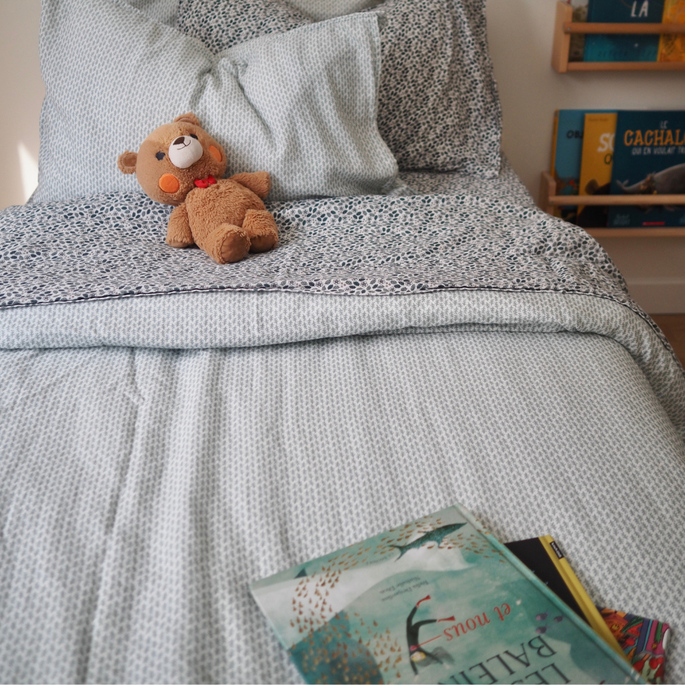 Ensemble de draps pour enfants en mousseline de coton Candide Living motif Flora vert sauge en vue rapproché d'un lit d'enfant. 