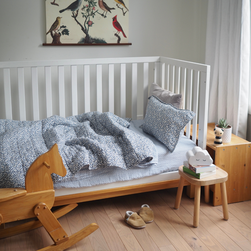 Ensemble de draps pour enfants en mousseline de coton Candide Living bleu chambray en taille junior dans une bassinette. 