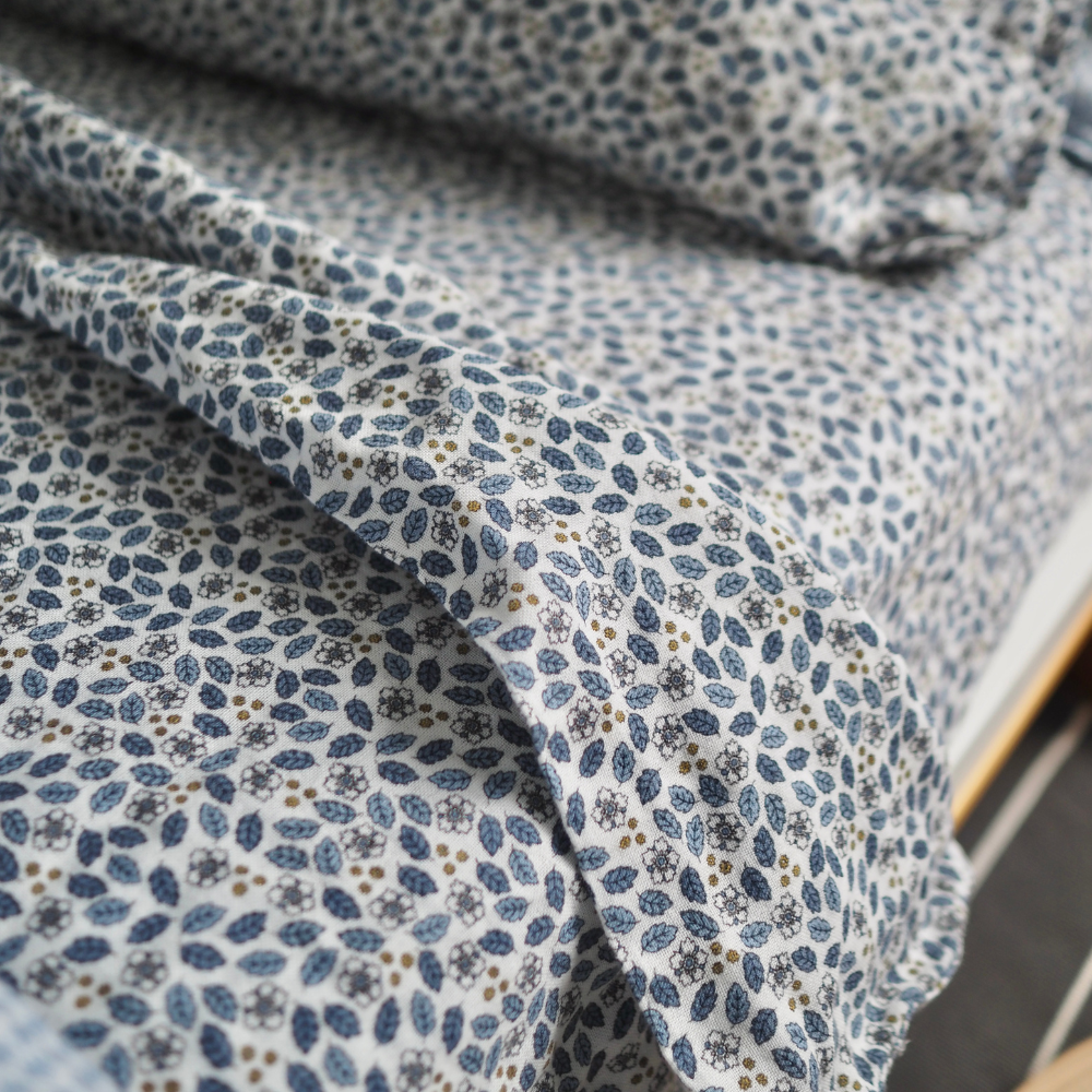 Gros plan sur l’ensemble de draps pour enfant en mousseline de coton Candide Living, motif Flora en bleu chambray.