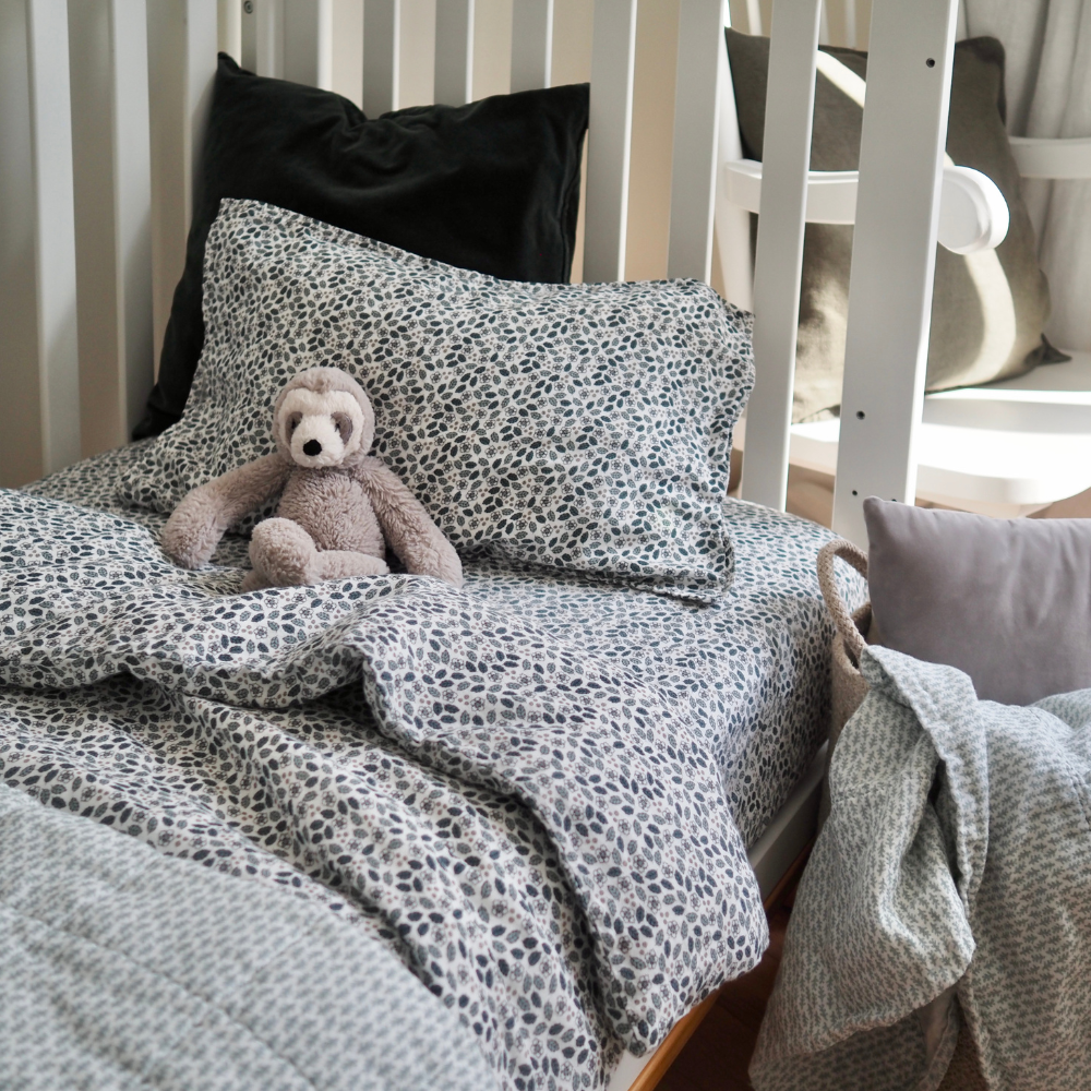 Ensemble de draps pour enfants en mousseline de coton Candide Living de motif Flora vert sauge dans une bassinette avec une peluche. 