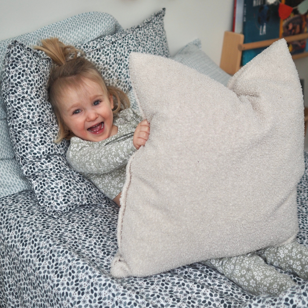Ensemble de draps pour enfants en mousseline de coton Candide Living de motif Flora vert sauge avec une petite fille souriante dans les draps. 