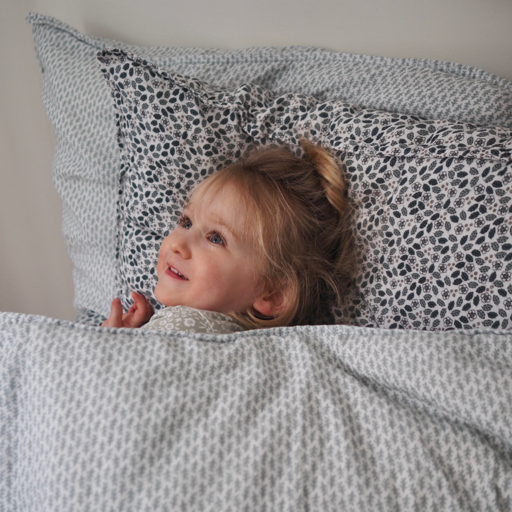 Ensemble housse de couette pour enfants en mousseline de coton Candide Living de motif Ondine en vert sauge avec une petite fille dans le lit. 